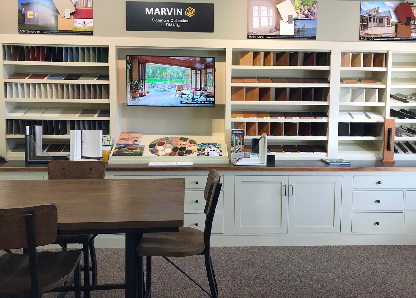 White and brown showroom with a table, TV, and shelves of paint and wood samples