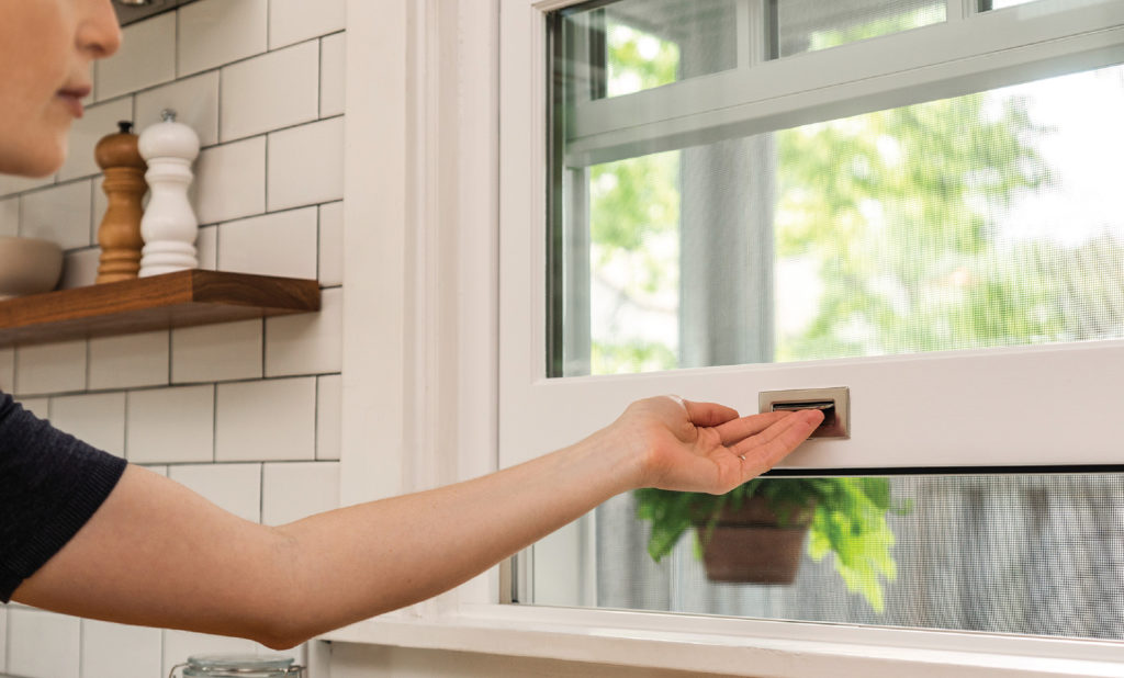 Womans arm lifting up a white framed window in a white kitchen