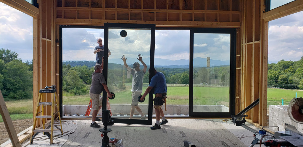Men working to put new floor to ceiling windows with black frames in the structure of a new house with mountains in the distance
