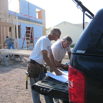 Two contractors working on a new house and looking over plans using trunk of car as a table