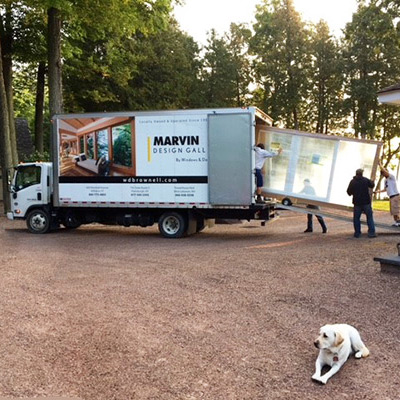 Men unloading new window from Marvin Design Gallery truck with yellow Labrador retriever in foreground